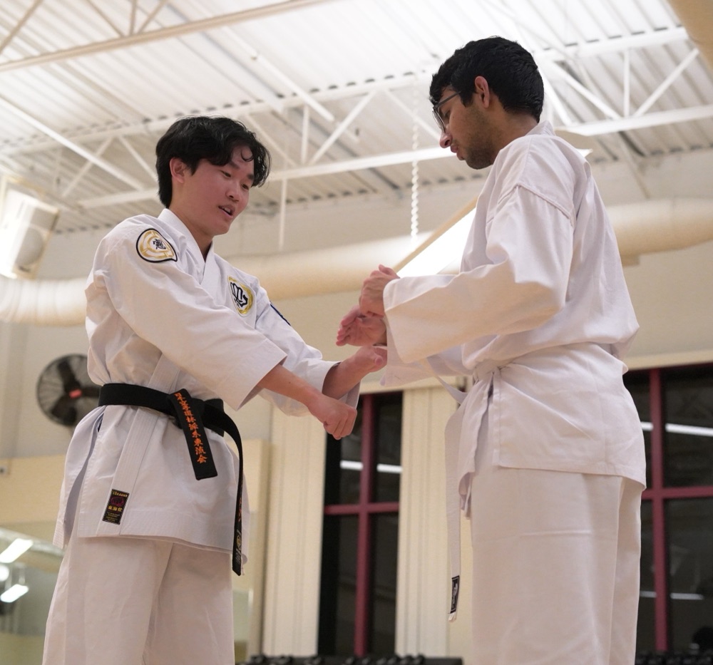 Gordon in a white gi and black belt correcting a white-belt student's technique