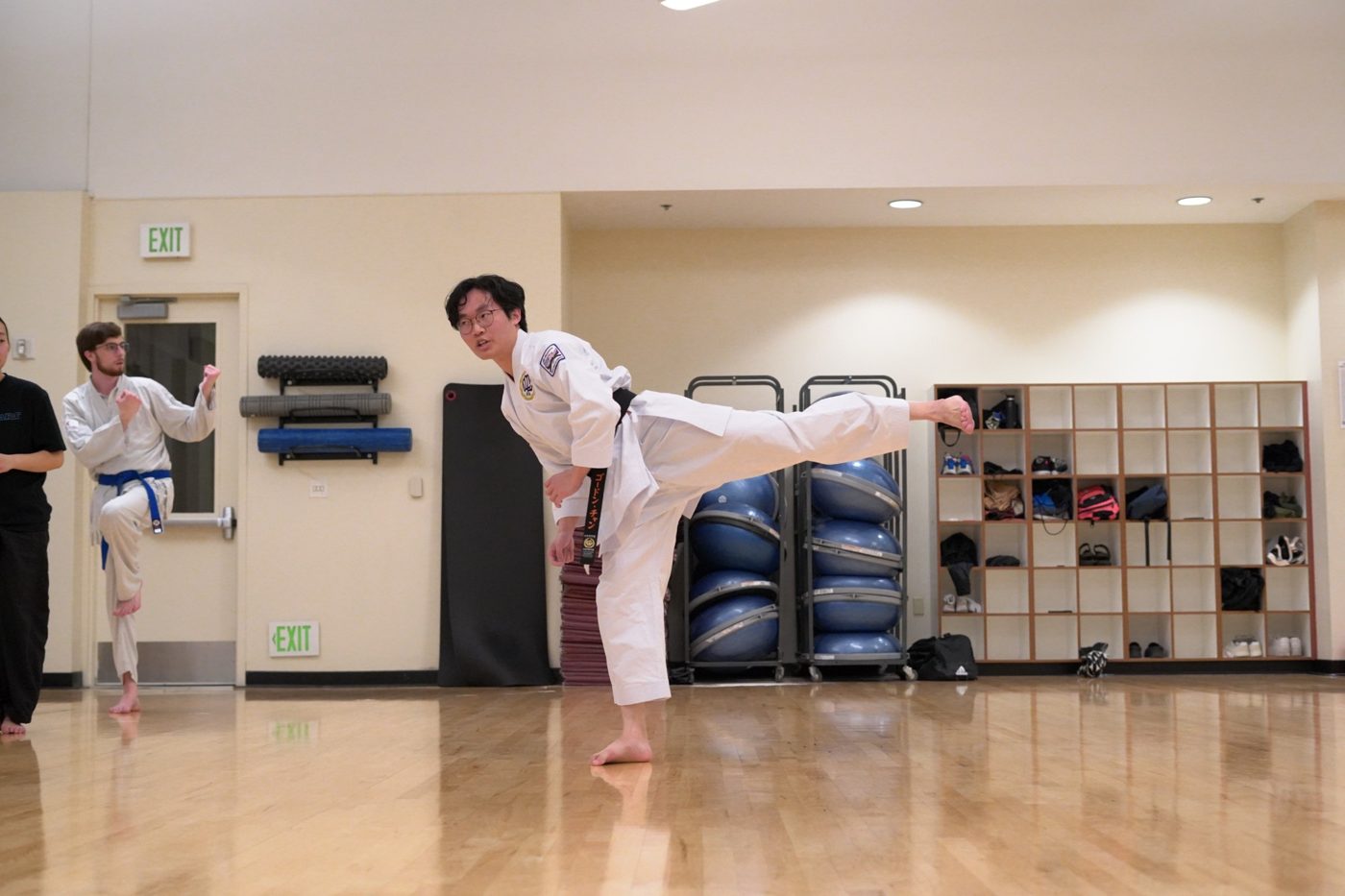 Gordon in a white gi and black belt demonstrating a side kick in a studio
