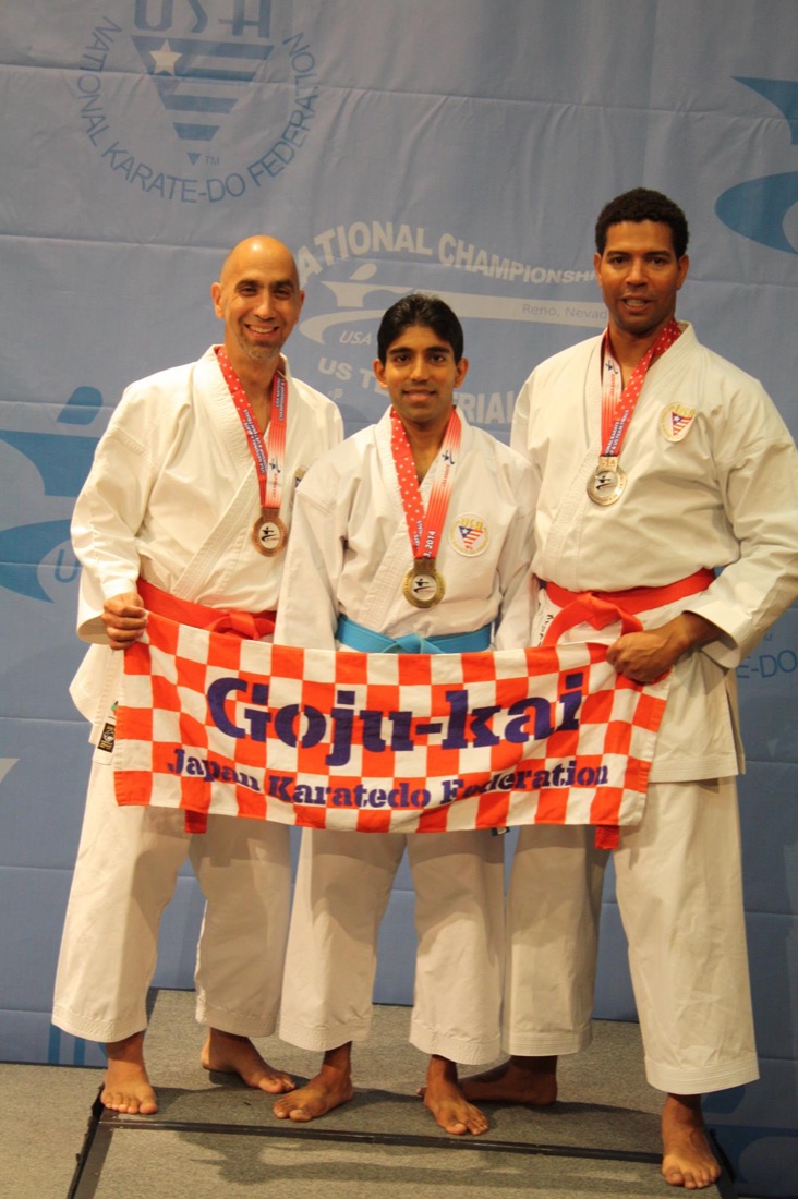 Three karate competitors on a podium with medals, holding a red-and-white Japan Karatedo Federation Goju-kai banner